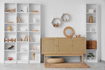 Interior of light living room with wooden commode and shelves