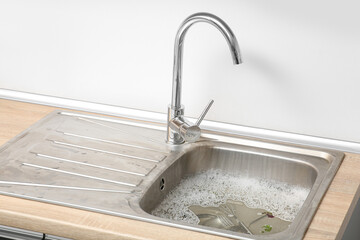 Metallic sink with soap water, dirty cutlery and food leftovers in kitchen, closeup