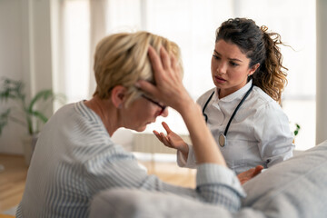 Fototapeta premium Female physician in white coat provides medical consultation to distressed patient at home. Professional healthcare visit showing empathetic medical support.