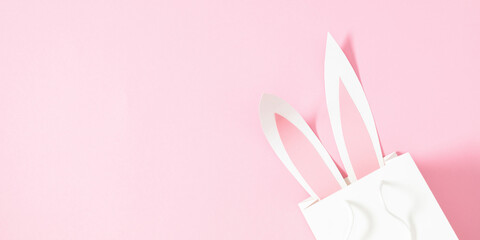 Cute Easter background with bunny ears in a gift bag. Simple Easter composition on pastel pink background, flat lay.