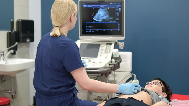 Doctor making abdominal ultrasound for boy using scanner machine. Female doc runs ultrasound sensor over patient tummy looking at screen. Medical examination of internal organs for school kids