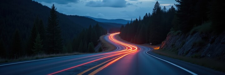 A winding road at dusk, illuminated by car lights, surrounded by lush forests and mountains, perfect for transportation and travel-themed projects.