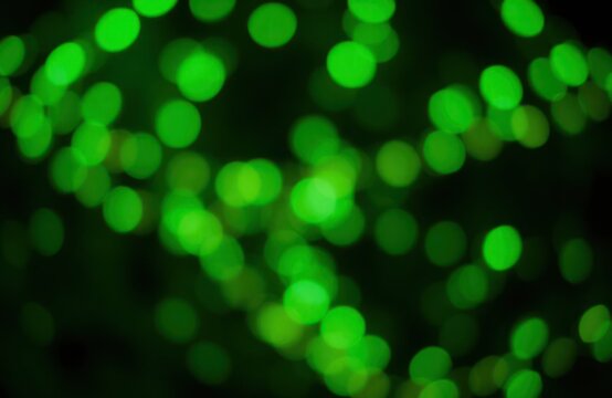 Green lights glow in dark night. Abstract urban scene. Dimly lit urban landscape at night. Illumination effect. Collection of green lights in darkness. Night time scene. Blurred city lights. Neon