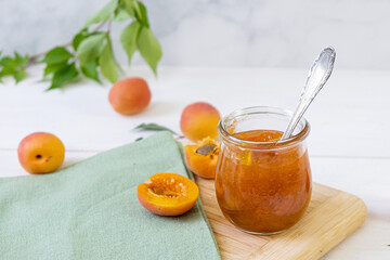 Homemade apricot jam in glass jar on kitchen white background. Summer harvest and canned food. 