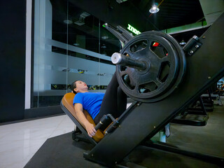 40 year old Asian Indonesian woman exercising with a leg press machine to train her leg muscles at...