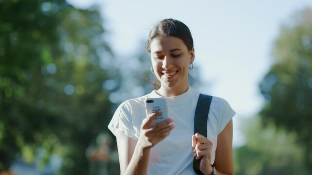 Young Hispanic Student Teen Girl Using Smartphone Outdoors in Sunlit Park