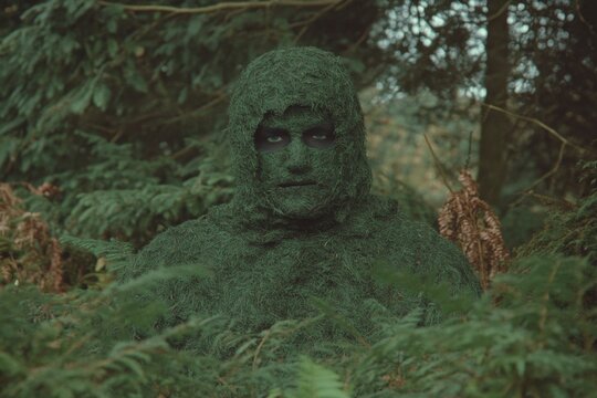 A hunter camouflaged in a ghillie suit blending seamlessly into the underbrush, observing wildlife from a distance