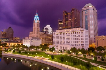 Fototapeta premium Twilight cityscape of downtown Indianapolis, Indiana, with illuminated buildings and parkland along the White River. Evening stroll. DOWNTOWN, COLUMBUS, OHIO, UNITED STATES