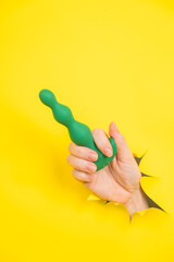 Naklejka premium Female hand with green anal plug sticking out of yellow paper background.