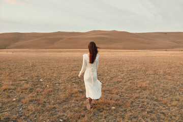 Woman walking through open field in white dress on sunny day for travel and beauty concept