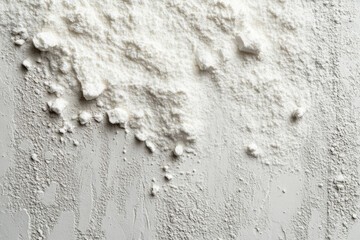 Fototapeta premium Pile of powder on white surface, spilled from container, with scattered particles around.