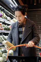 Woman Selecting Fresh Produce at a Supermarket with a Shopping Cart