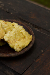 Tempe Mendoan, or Tempe Tepung, is thinly sliced tempeh coated in seasoned wheat flour batter and briefly fried to golden perfection. A classic Indonesian snack, served warm on a rustic wooden table.