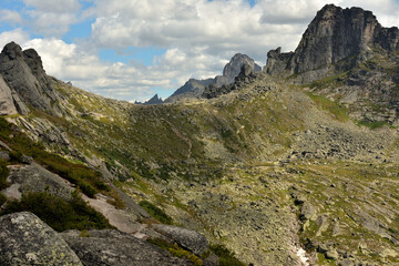 Saddle of a steep mountain pass surrounded by high rocks with pointed peaks on a cloudy summer day.