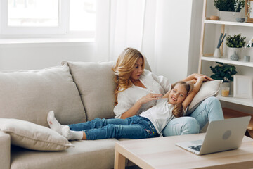 Mother and daughter bonding over technology, sitting on a cozy couch and exploring the world on a laptop together