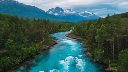 Drone high-angle photo of the turquoise-colored mountain river flowing in the pine woodland with a view of the mountain peaks in the background in Innlandet County, Norway