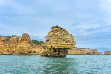 Fototapeta premium At dusk, Golden coastal cliffs rising above emerald waters with intricate sea caves. Features stunning rock formations shaped by waves, Algarve, Portugal.
