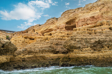 Fototapeta premium At dusk, Golden coastal cliffs rising above emerald waters with intricate sea caves. Features stunning rock formations shaped by waves, Algarve, Portugal.