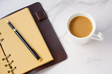 ミルクをたっぷり入れたコーヒー、カフェ・ラッテを飲みながら、茶色の革のシステム手帳でデスクワークをしているイメージ
