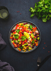 Mexican style salad with tuna, avocado, corn, beans, tomatoes and cilantro, black background, top view