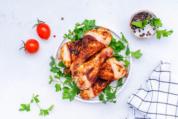 Baked chicken legs or drumsticks in spices with parsley on plate, white table background, top view