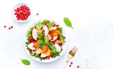 Winter persimmon salad with grilled chicken, pomegranate, walnuts, oranges and lettuce, white background, top view