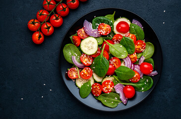 Healthy vegetable salad with spinach, tomatoes, cucumber and red onion. Black table, top view