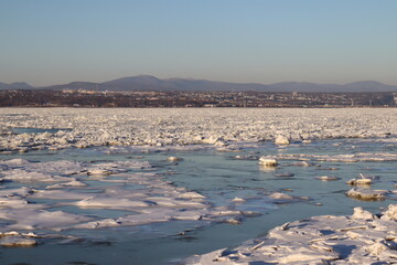 A coastline and a river with icebergs. Pieces of icebergs and the St-Laurent river in Quebec and in winter. A riverside background in winter. A shore in Quebec city and December calendar.
