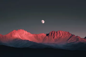 Poster Photograph of a red mountain range with a moon in the dark sky, with light pink and gray hues.