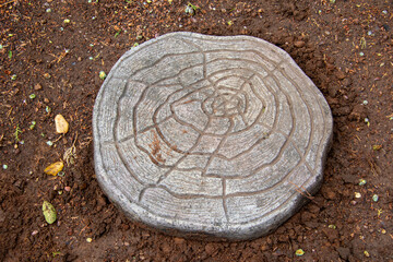 A cement art stepping stone isolated on a patch of wet soil in a garden