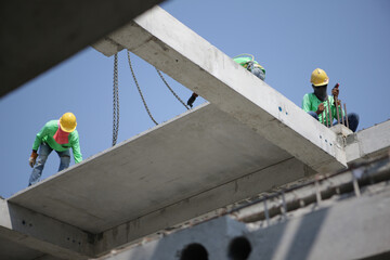Fototapeta premium Construction crane lifting concrete slab with workers on scaffold
