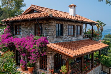 Stone house with terracotta roof, vibrant bougainvillea, and sea view.