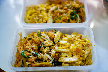 Photo of vegetarian Pad Thai in lunch boxes arranged on a kitchen table in a home kitchen.