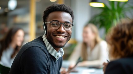 Smiling young professional: A portrait of a happy and confident young African American man, wearing glasses and earbuds, smiles warmly at the camera in a vibrant coworking space.  