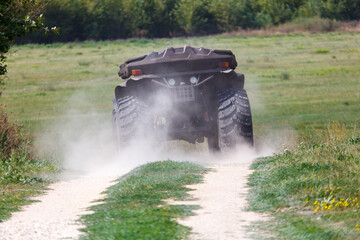 A large, dirty, muddy, and dusty monster truck is driving down a dirt road © schankz