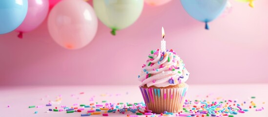 Birthday cupcake with candle and pastel balloons.