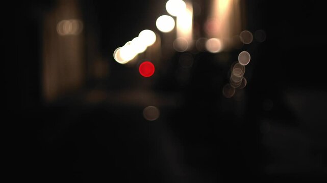 Dimly lit street at night with parked cars and glowing streetlights in focus pull shot