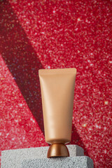 Plastic tube for cream or lotion. Skin care or sunscreen cosmetic with stylish props on red background