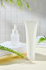 An advertising image for beauty products with natural extract, in a bathroom background. A white tube and a white dropper bottle mockup placed on a tray, with towels, tea trees, and fern branches.