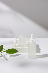 Advertising photo for skin care products, two glass serum bottles without labels placed on a white podium with green tea leaves. Green tea extract has moisturizing and acne prevention properties.