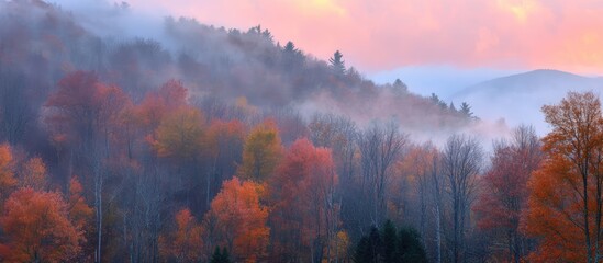 Fototapeta premium Serene autumn landscape with morning mist enveloping vibrant mountain foliage under a colorful sunrise sky.