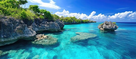 Obraz premium Turquoise waters and rocky coastline create a stunning tropical island paradise scene under a bright blue sky.