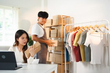 Asian women are looking at laptop computers to check orders, with cardboard boxes and goods all around, selling products online from home. being a new normal online business.