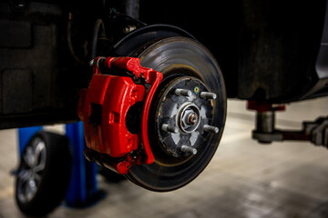 The braking system of the car with the wheel removed with the disc, pads, red hub and cooling holes during maintenance and replacement in the workshop on the vehicle repair