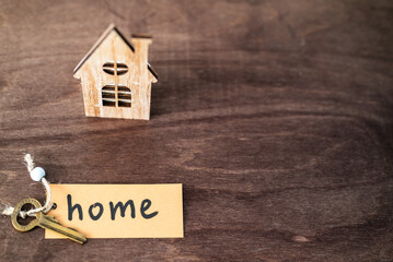 wooden house representation and a key with a key chain with the word home on it - buying and selling house concept
