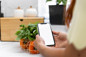 Hand with white screen phone near fresh vegetables and fruits in a reusable bag in the modern...