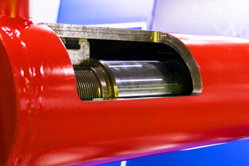 A hydraulic cylinder in cross-section. The internal structure of the cylinder is visible: piston, rod, sleeve, and other elements. The cylinder is painted red.