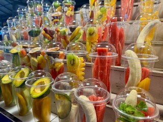 Assorted fresh fruit cups in clear containers on a market stall display, colorful and vibrant, representing healthy eating and freshness