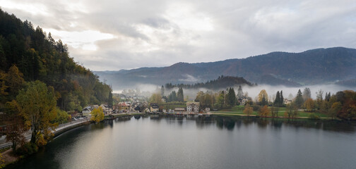 Fototapeta premium Drone aerial view of lake Bled embraced by autumn colors and misty mountains in slovenia