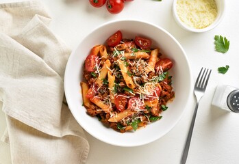 Bowl of bolognese penne pasta with minced meat, tomatoes and greens